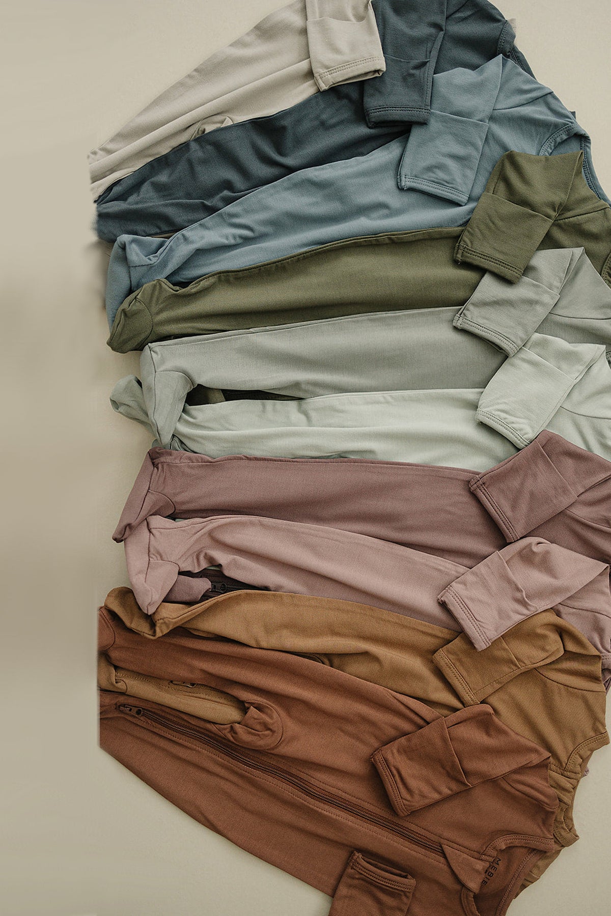 A variety of colorful baby footed zipper pajamas made from soft bamboo fabric, neatly folded on a beige surface.