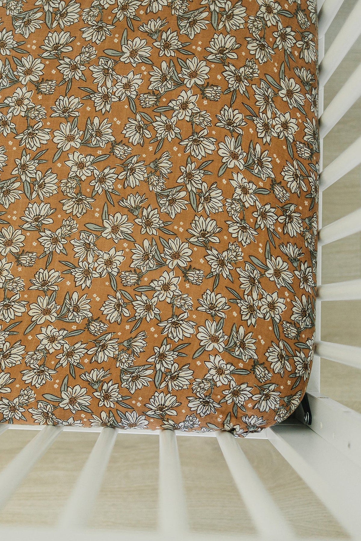 Floral-patterned crib sheet with white magnolias on a brown background, fitted on a white crib mattress.