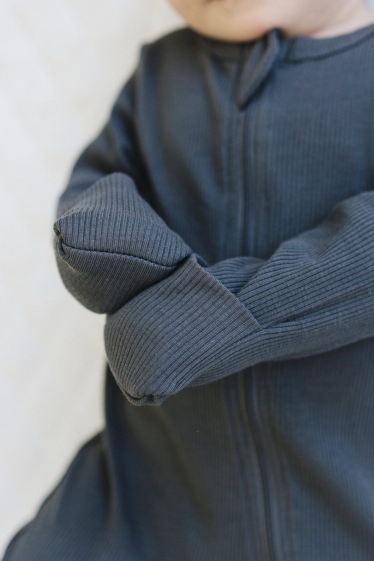 A baby wearing charcoal ribbed pajamas with a zipper, crafted from organic cotton, shown in a close-up view.