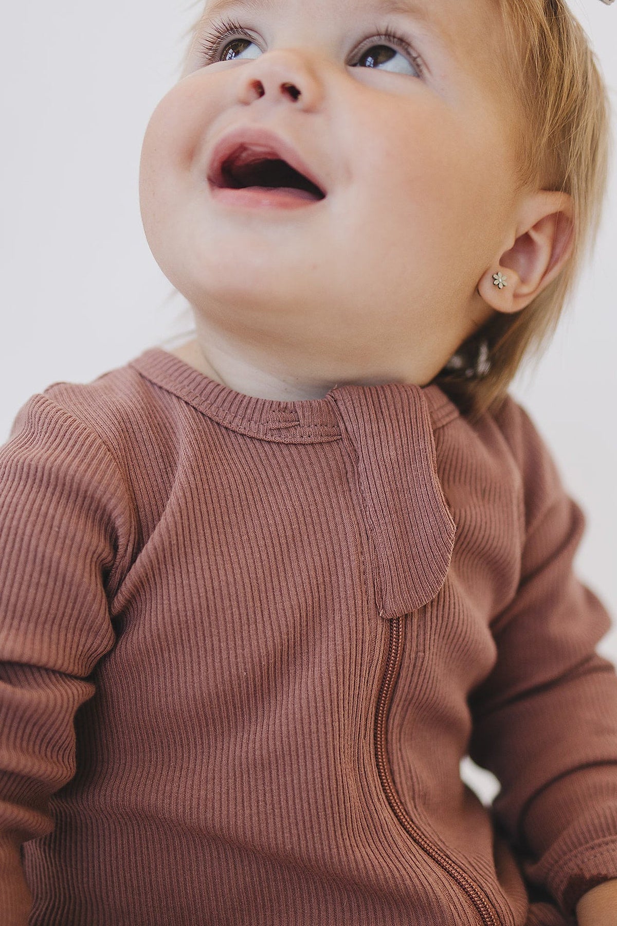 A baby wearing a dusty rose ribbed zipper pajama looks upwards, showcasing the organic cotton fabric.