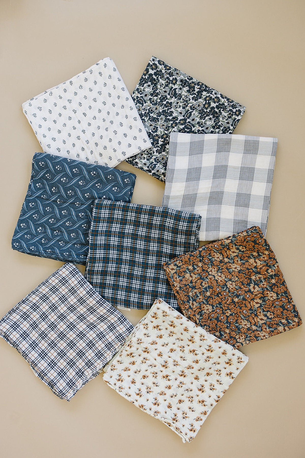A selection of eight patterned muslin burp cloths in various plaid and floral designs, arranged on a beige background.