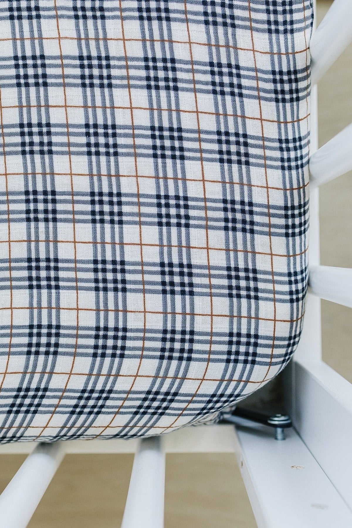 A vintage plaid muslin crib sheet with blue and brown lines on a white background, covering a crib mattress.