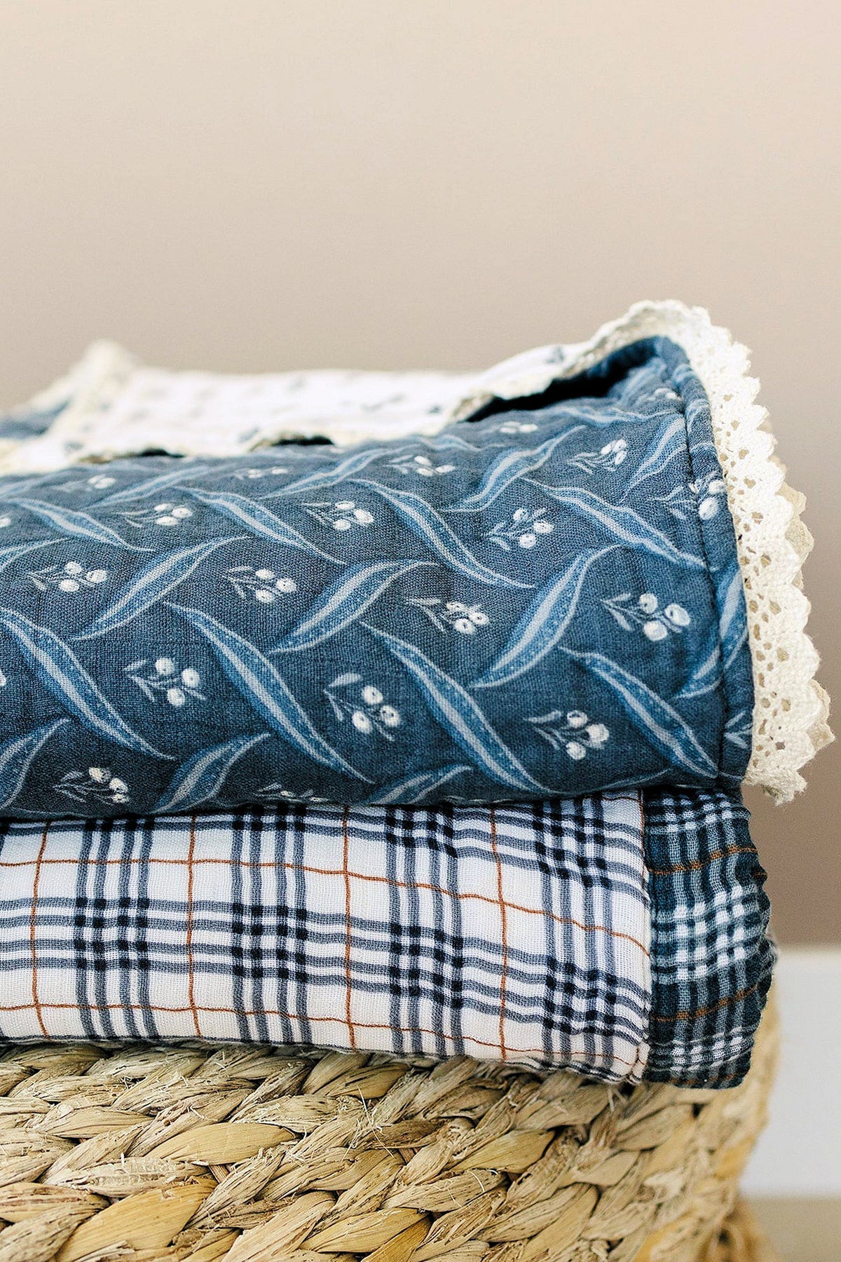 A navy quilt with berry patterns and lace trim sits atop a checked fabric, resting on a woven basket.