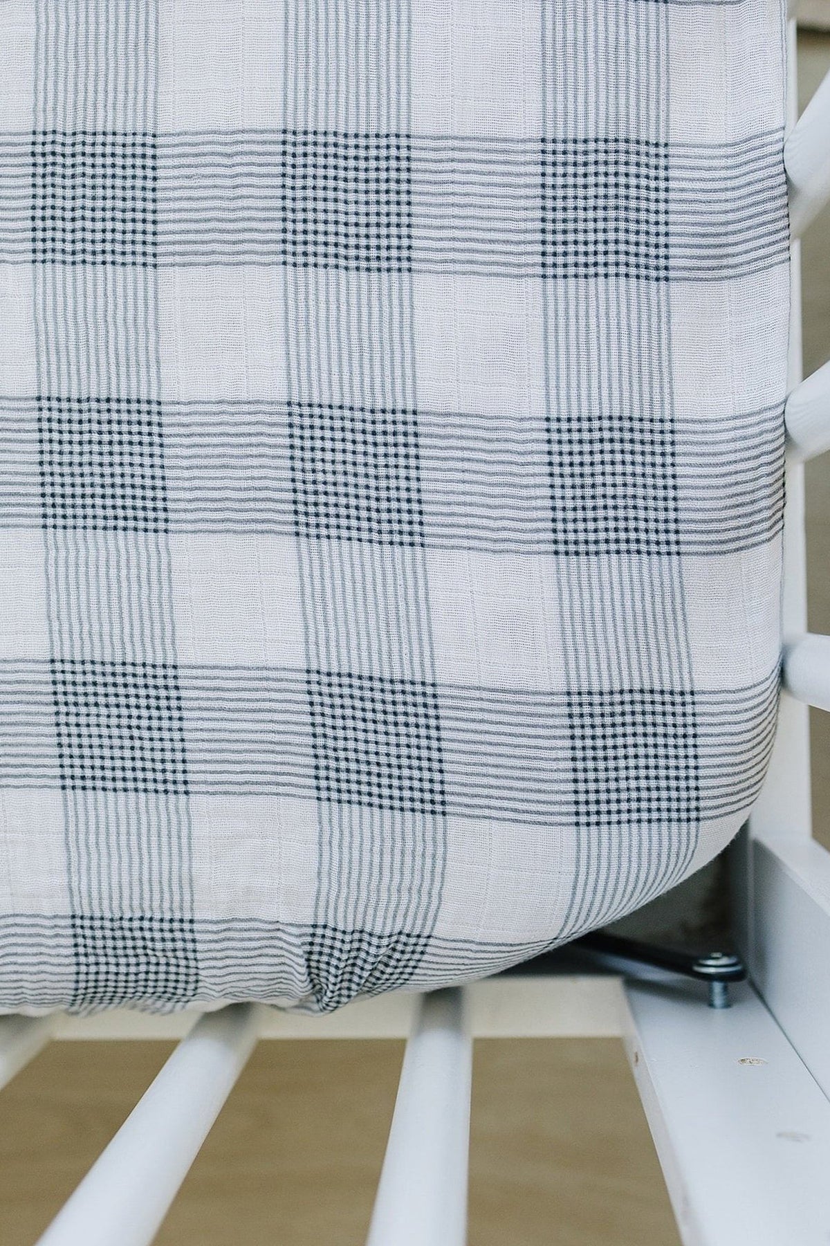 Close-up of a coastal plaid muslin crib sheet in soft white and gray tones, fitted snugly around a crib mattress.