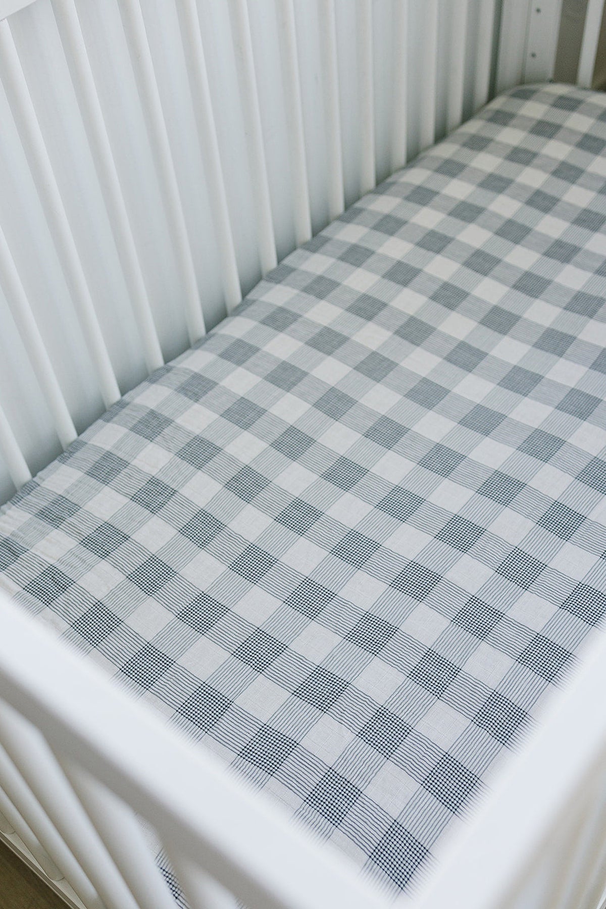A white crib with a coastal plaid muslin crib sheet featuring alternating gray and white squares.