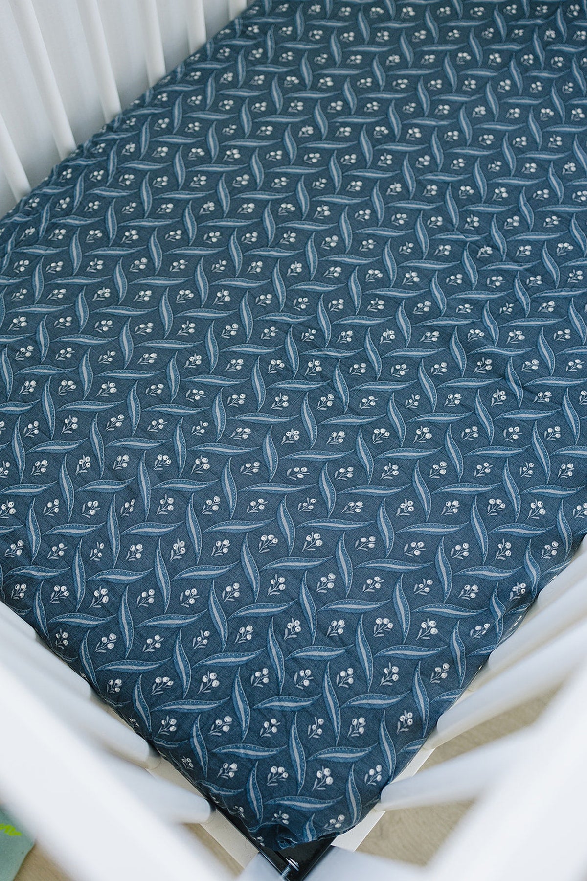Navy crib sheet featuring a delicate white floral pattern, made of soft muslin fabric, inside a white crib.