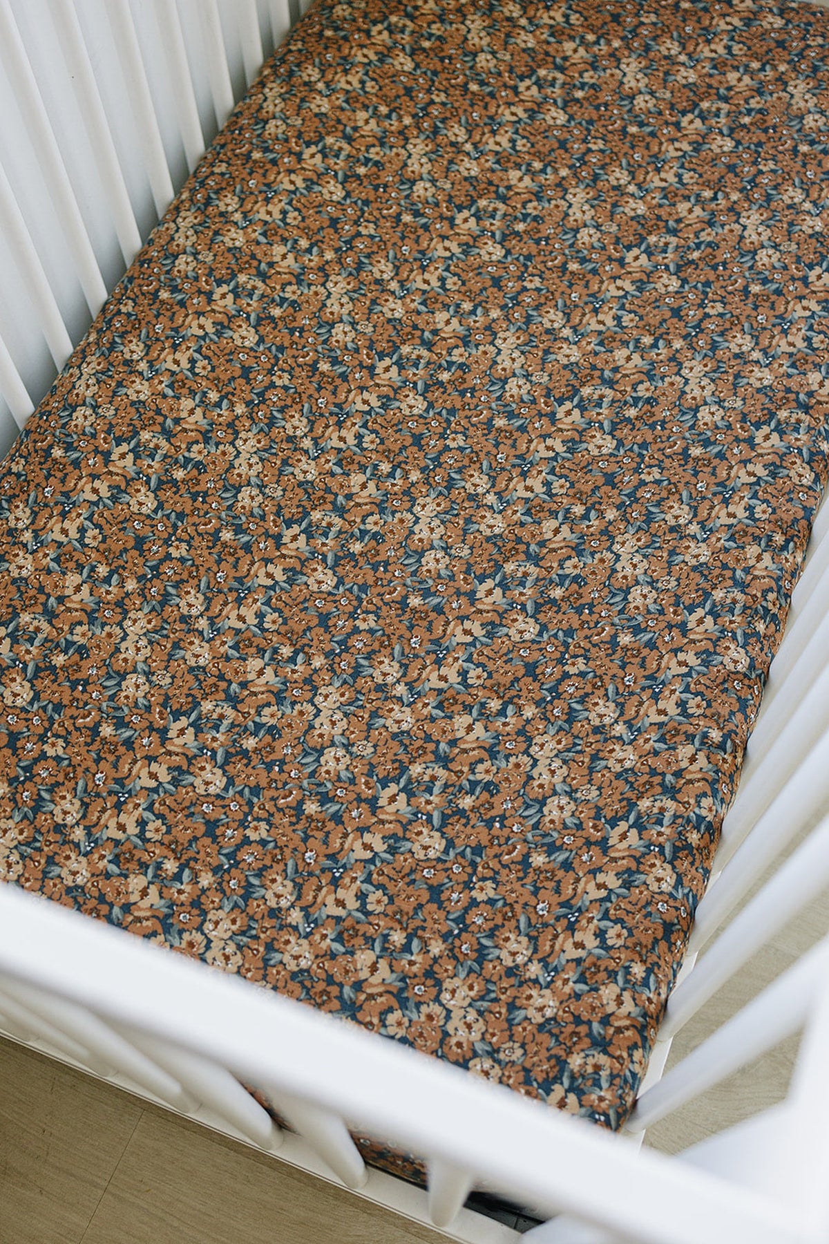 Floral-patterned crib sheet in warm brown and blue tones, fitted on a white crib mattress.