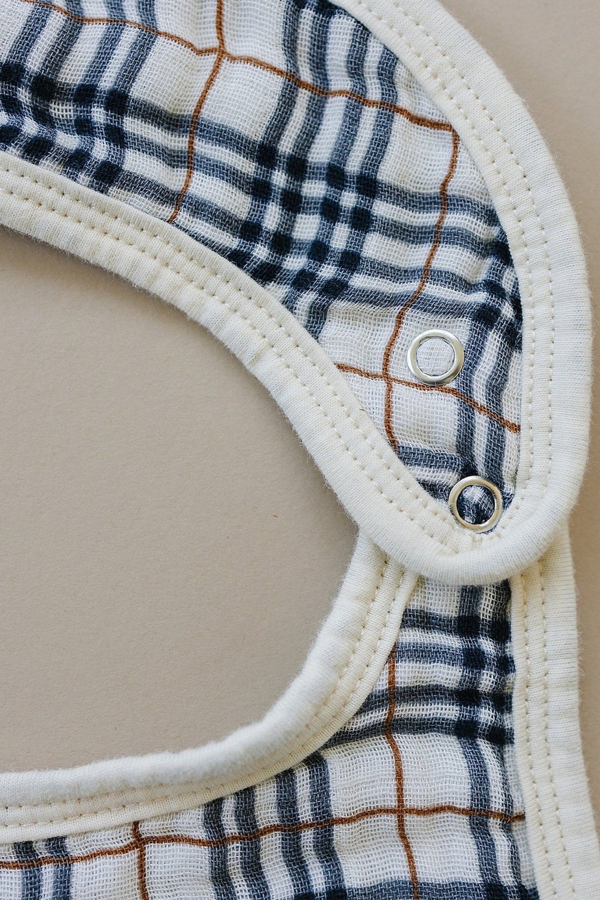 Close-up of a Mebie Baby muslin bib in vintage plaid with snap closures, featuring blue and brown stripes.