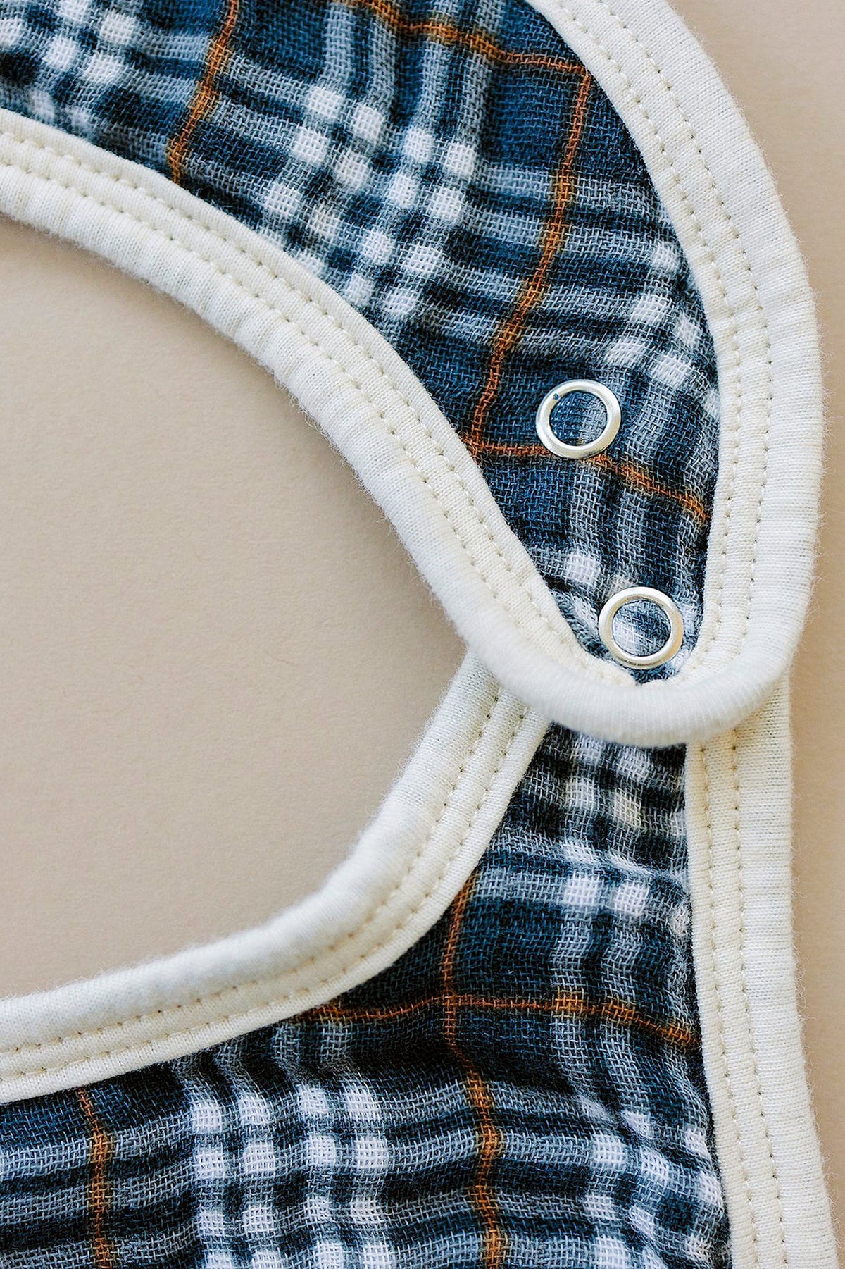 Navy plaid muslin bib with white trim and snap closures, designed for babies. Made from soft, absorbent cotton.