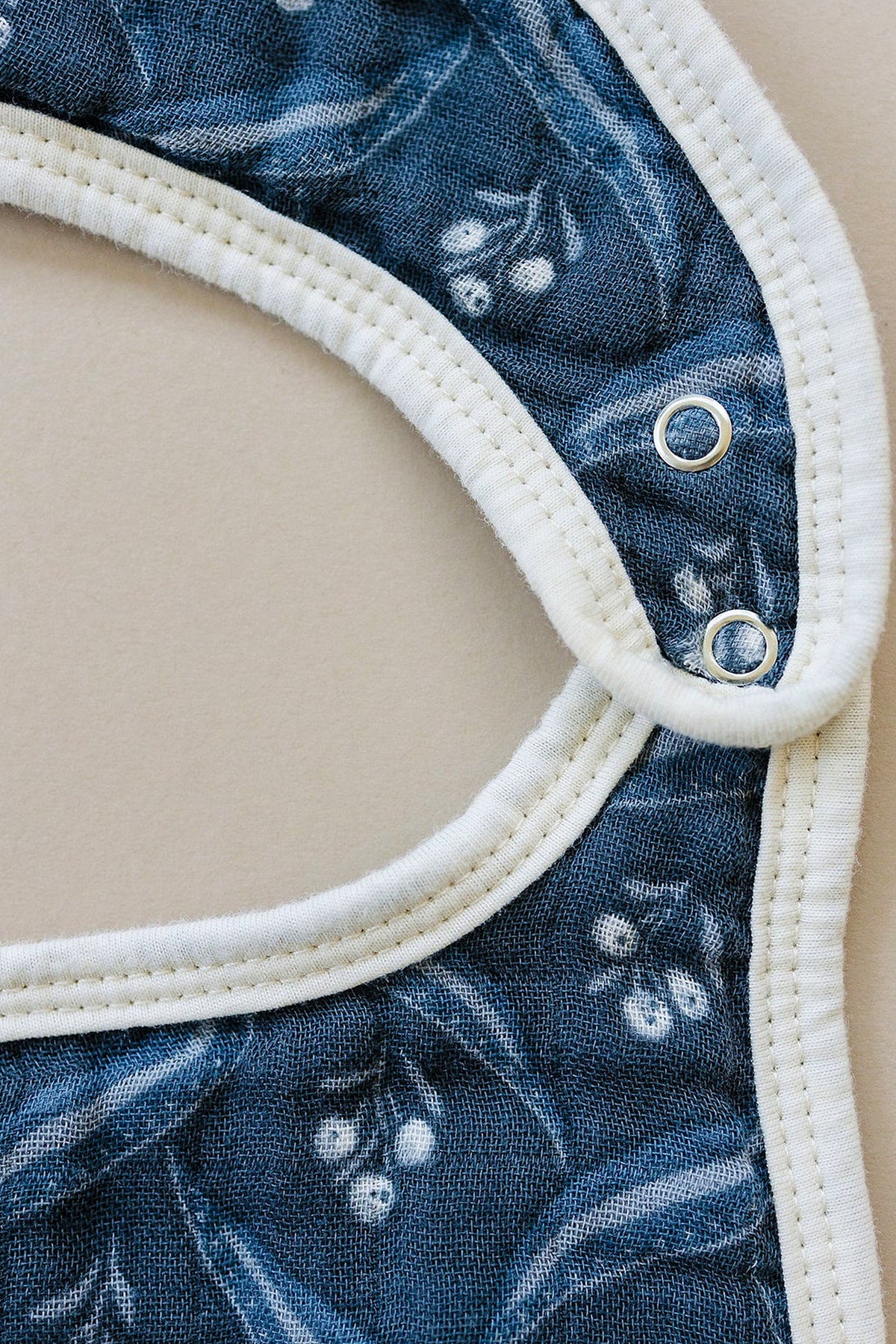 Close-up of a navy blue muslin bib with white berry pattern, featuring white trim and snap closures.