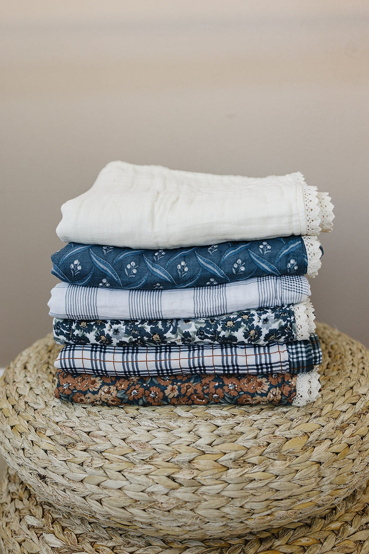 A stack of colorful, patterned muslin quilts with lace edges on a woven basket.