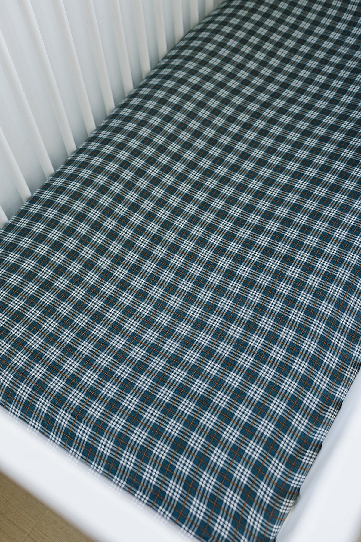 Navy plaid muslin crib sheet covers a mattress in a white crib, showcasing a checkered pattern.