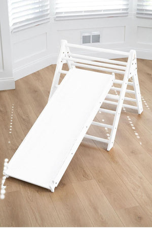 A white wooden Pikler triangle with a slide attached, set on a light wooden floor in a bright room with natural light. Ideal for active play and safe indoor adventures.