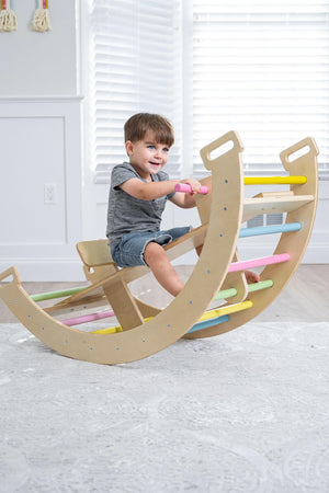 A young child joyfully plays on a wooden Bailis climbing arch that doubles as a rocker, featuring colorful grips. The bright, airy room has white walls and natural light streaming.