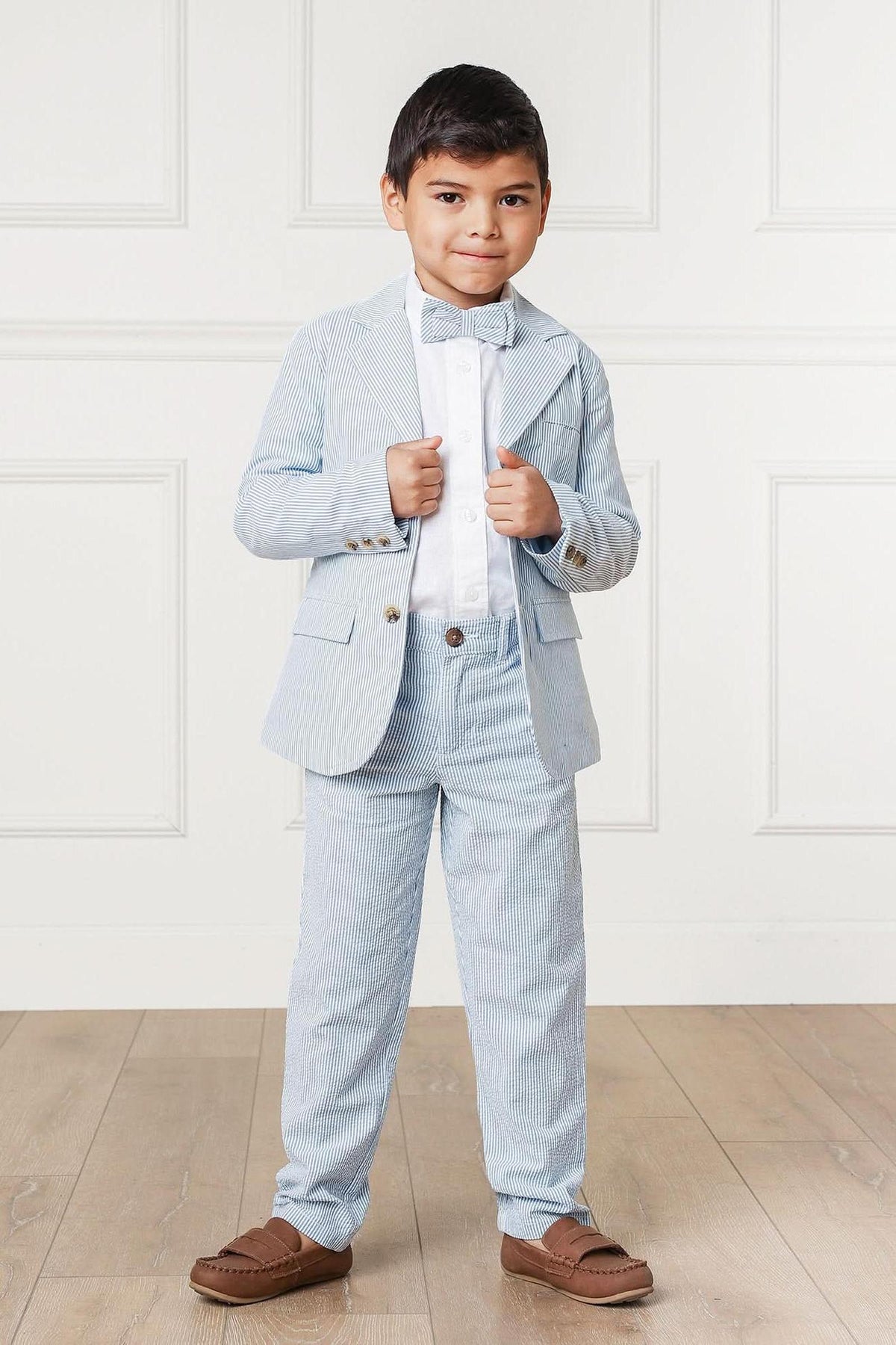 A young boy stands confidently in a light blue seersucker suit, complete with a bow tie and white shirt.