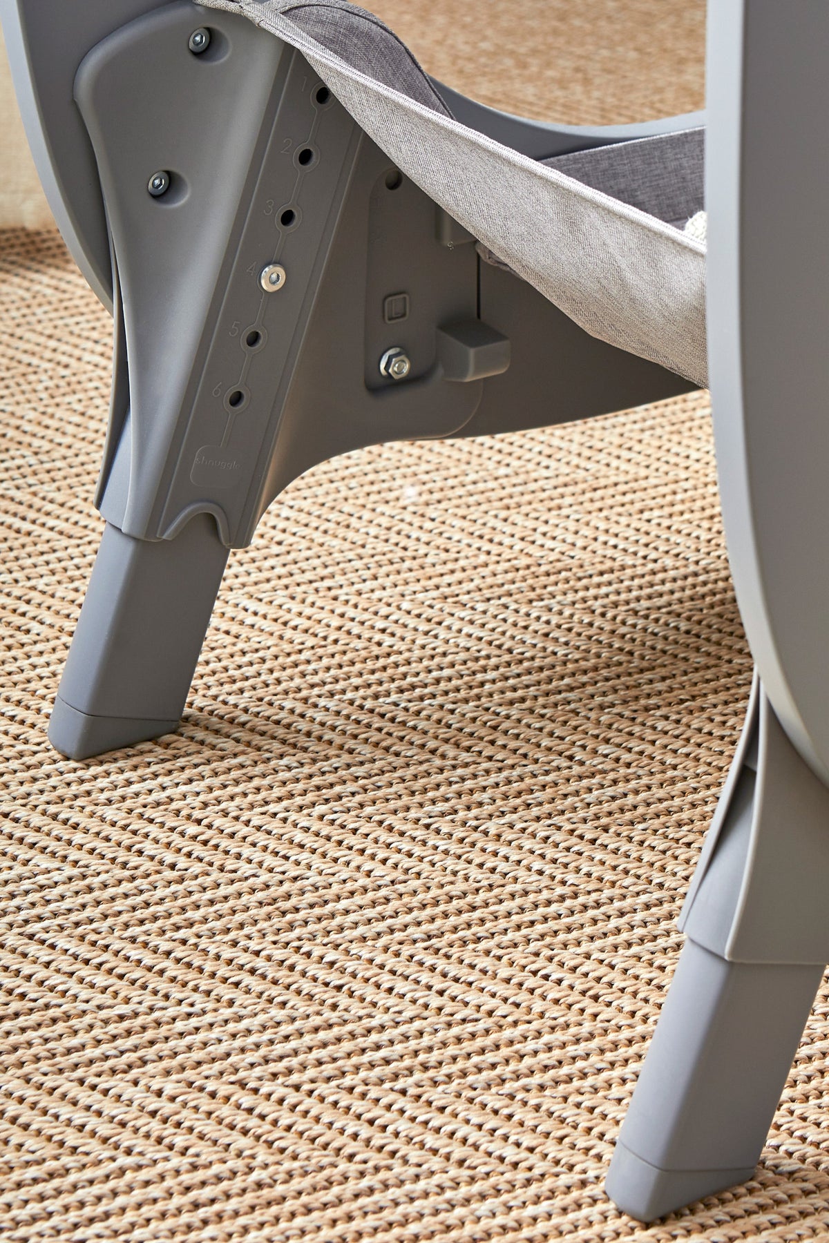 Close-up view of the Shnuggle Air Lite Bedside Bassinets sturdy grey plastic legs, showcasing its modern design and adjustable height feature. The bassinet is set on a textured woven surface.