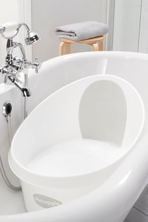 White Shnuggle Toddler Bath Tub inside a larger bathtub, with chrome faucet and a folded towel on a stool.