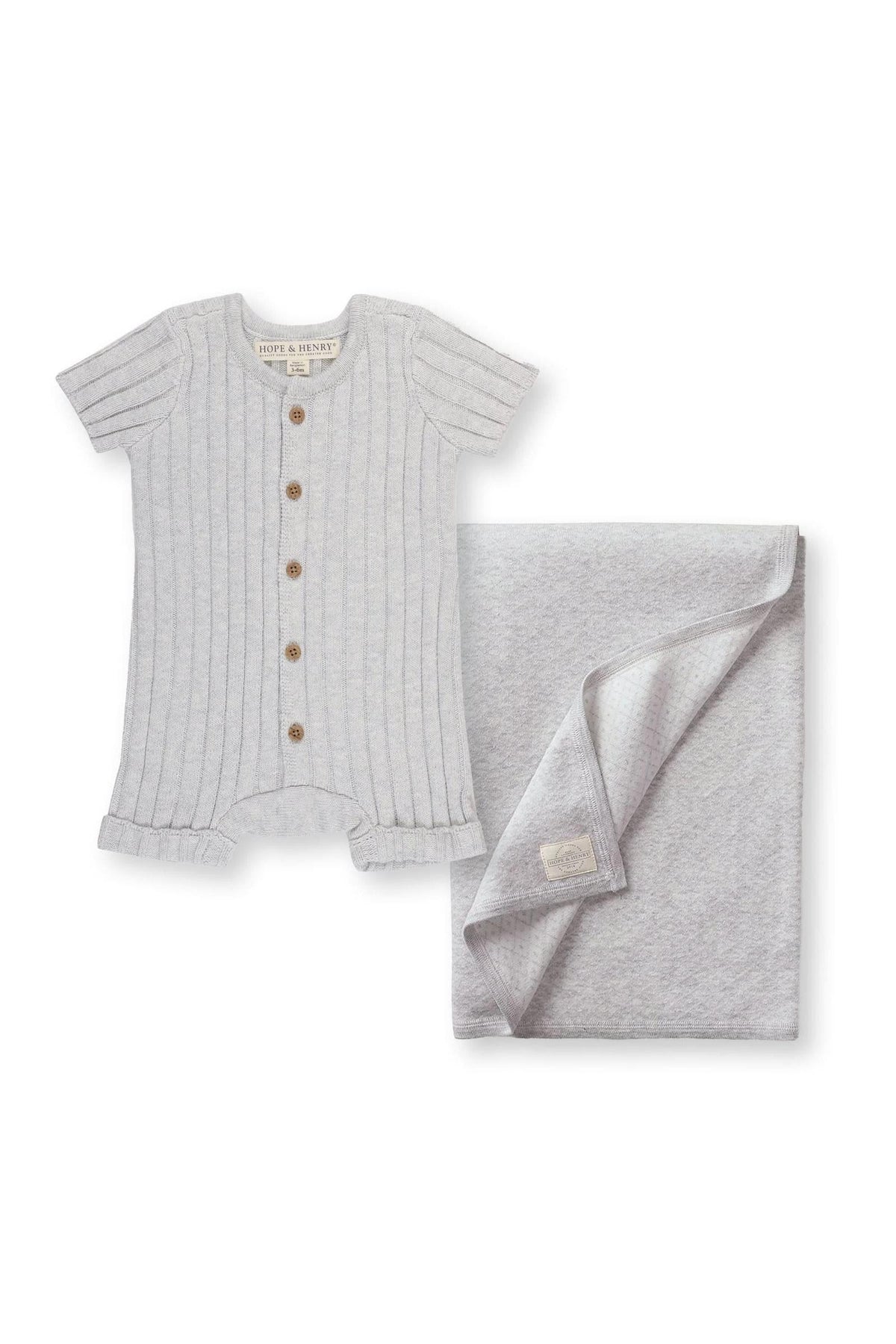 A light grey organic cotton shortie romper with a button-front closure is displayed alongside a matching jacquard blanket. Both pieces are designed for newborns, emphasizing comfort and style.