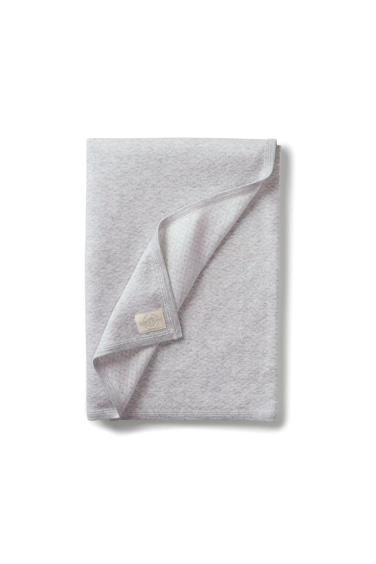 A soft, lite grey jacquard blanket made from organic cotton, featuring a textured design and a small brand label. Ideal for newborns, it emphasizes comfort and sustainability.