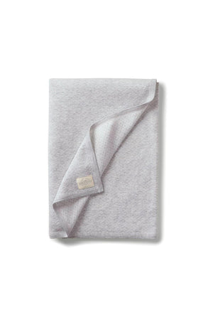 A soft, lite grey jacquard blanket made from organic cotton, featuring a textured design and a small brand label. Ideal for newborns, it emphasizes comfort and sustainability.