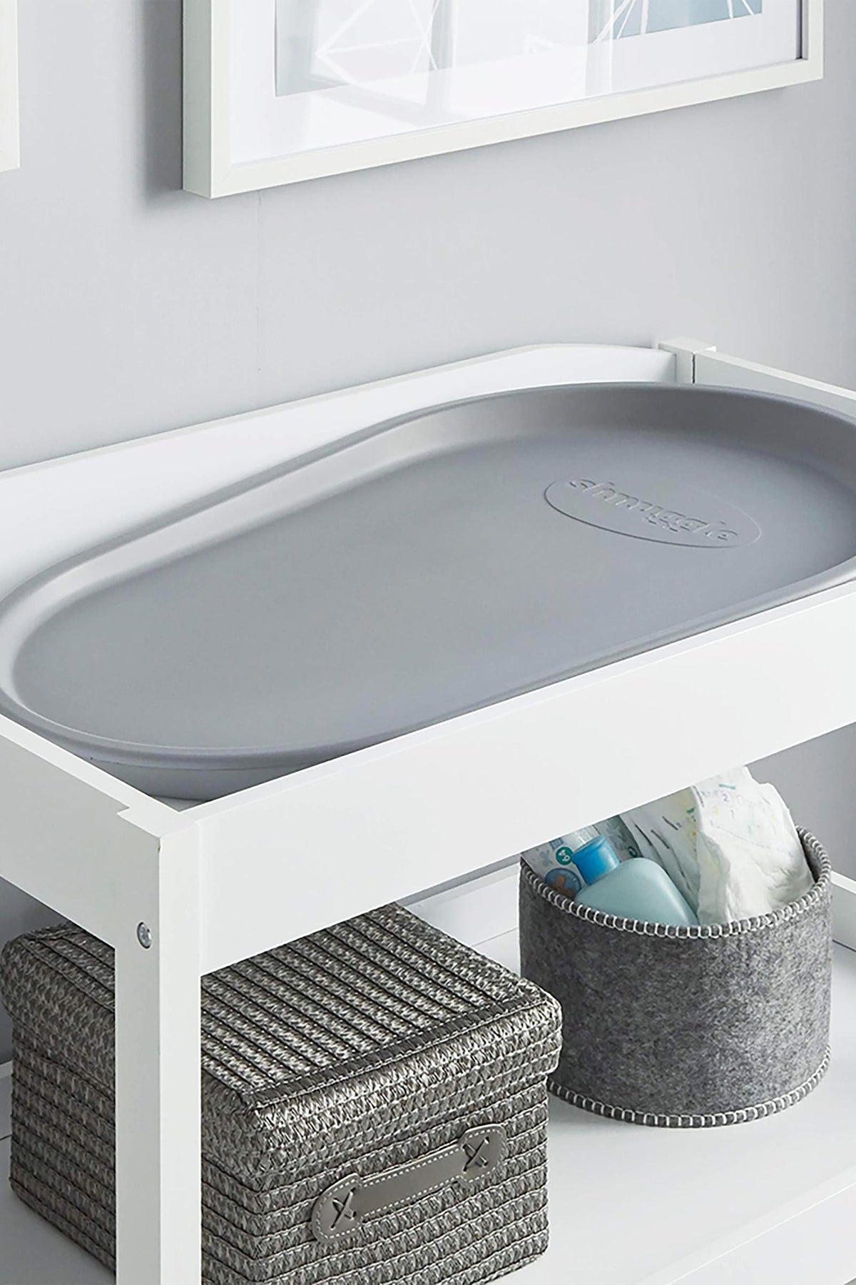 A gray Shnuggle changing mat on a white table with wicker and felt storage baskets underneath.