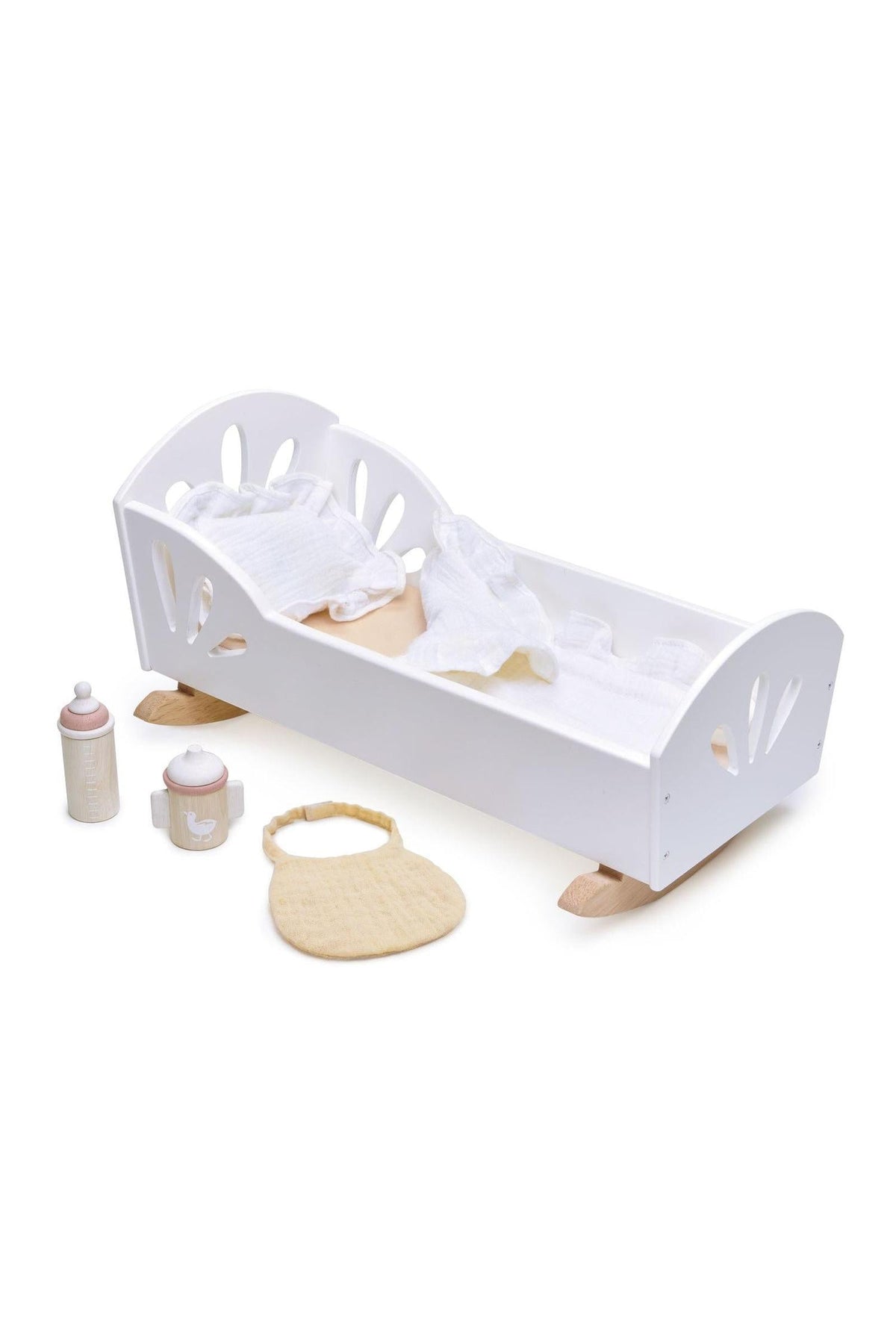 White wooden dolly bed with natural rockers, accompanied by toy bottle, cup, and bib on a white background.