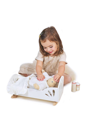A child plays with a doll in a white wooden dolly bed, accompanied by toy bottles on the side.