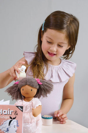 A young girl with long brown hair styles a dolls hair, using a small bottle. The scene features soft colors and a playful atmosphere, showcasing imaginative role play.