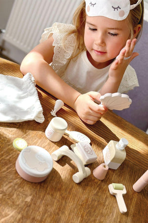 A girl examines a shell-shaped mirror among various wooden spa accessories on a wooden table, featuring soft pastel colors.