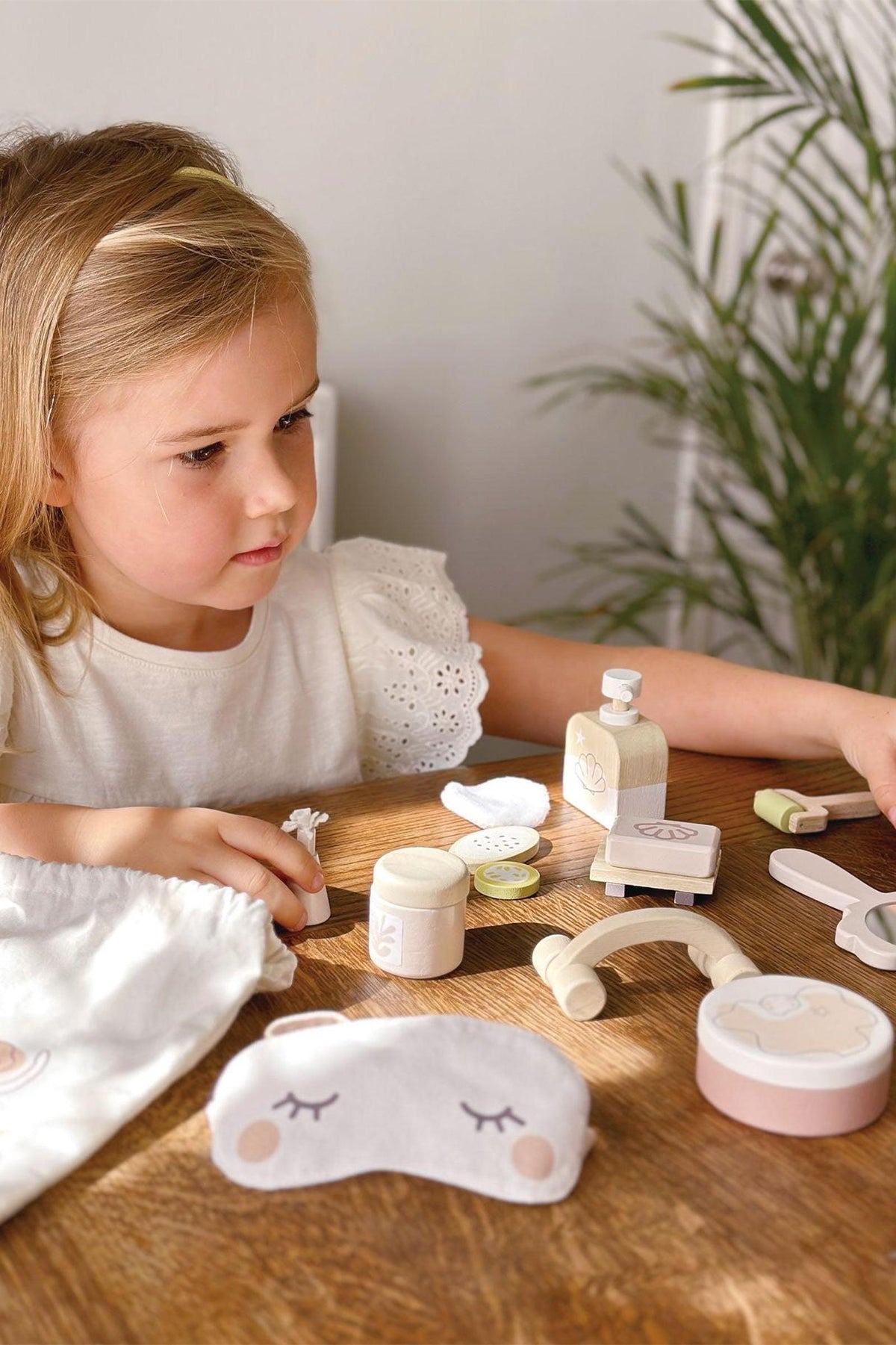 A young girl engages with the Tender Leaf Wooden Toys Spa Retreat Set on a wooden table, surrounded by spa-themed.