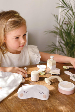 A young girl engages with the Tender Leaf Wooden Toys Spa Retreat Set on a wooden table, surrounded by spa-themed.