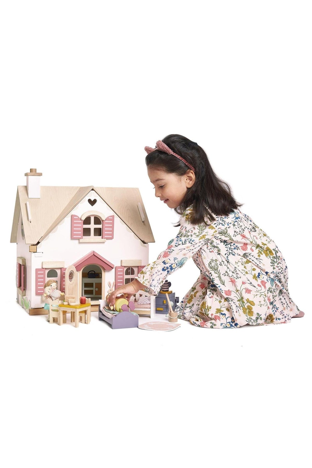 A young girl plays with a wooden dollhouse, arranging furniture and characters outside the charming, pastel-colored Cottontail Cottage.