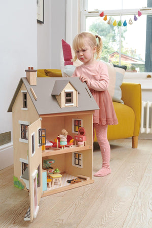 A young girl interacts with a wooden dollhouse, featuring a neutral facade and colorful interior accessories, in a bright living.