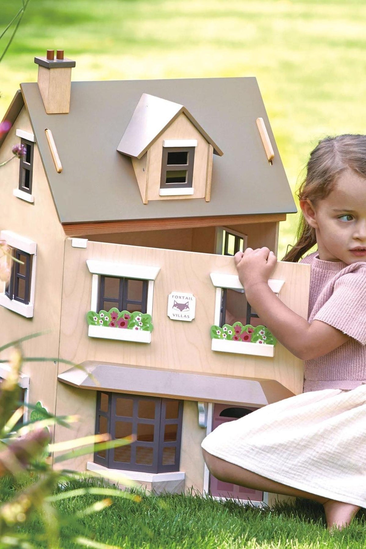 A child interacts with the Tender Leaf Foxtail Villa dollhouse, showcasing its stylish wooden design and colorful flower boxes.
