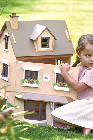 A child interacts with the Tender Leaf Foxtail Villa dollhouse, showcasing its stylish wooden design and colorful flower boxes.