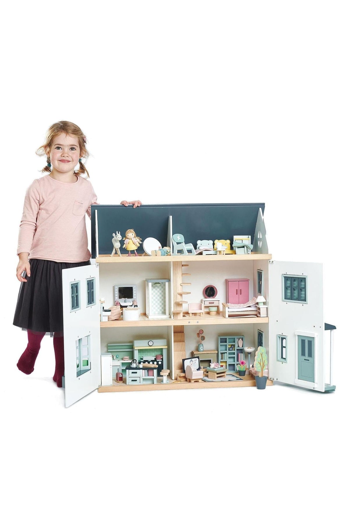 A young girl proudly holds a colorful wooden dollhouse, showcasing multiple rooms with detailed furniture.