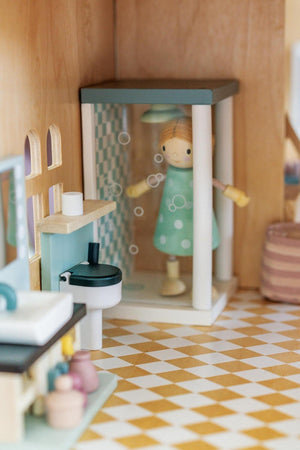 A charming bathroom scene inside a wooden dollhouse features a shower with bubbles, a colorful doll in a polka-dotted dress, and a stylish sink.