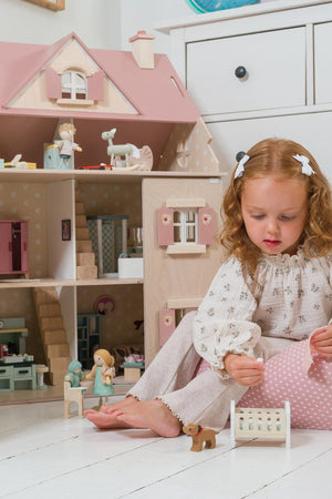 Young girl playing with a dollhouse and toys on a white floor.