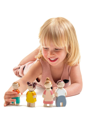 A young girl smiles while playing with four colorful wooden family figures, showcasing imaginative play and engagement.