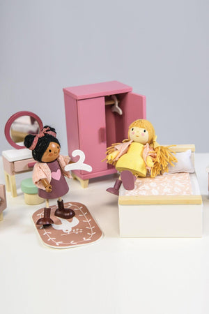 Two charming dolls interact in a colorful dollhouse bedroom, featuring a wooden wardrobe, bed, and decorative rug.