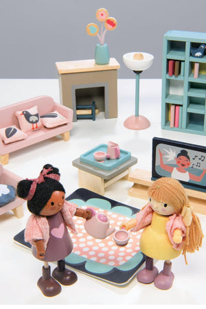 Two wooden dolls engage in a tea party setting with colorful furniture, a coffee table, and decorative accessories.