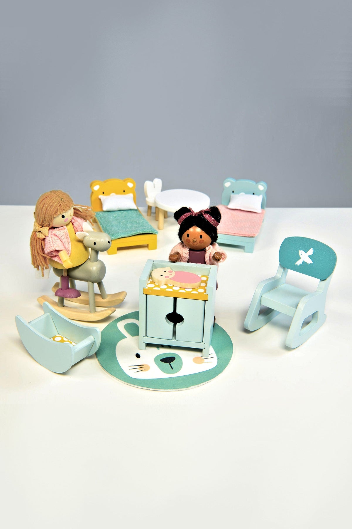 A colorful wooden toy set featuring dolls, a rocking horse, beds, and a playful rug, designed for imaginative play.