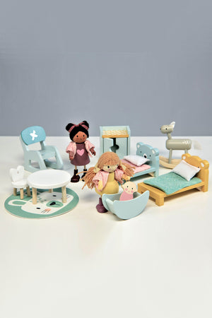 A colorful wooden dollhouse nursery set features two dolls, a crib, rocking horse, table, chair, and rug.