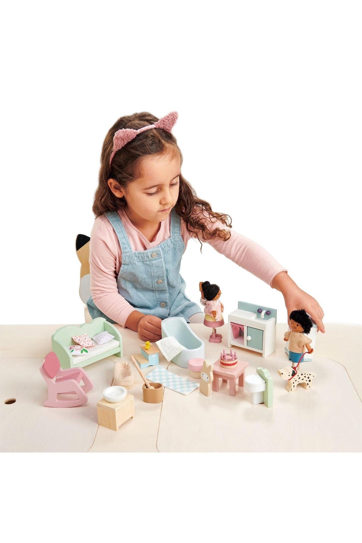 A child playing with a Tender Leaf wooden dollhouse furniture set, including miniatures like a bathtub, sofa, and figures.