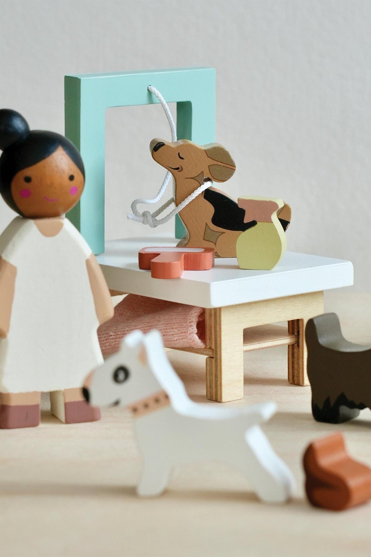 A wooden play set features a groomer figure attending to playful dogs, including a corgi and a small white dog. The scene is colorful and designed for imaginative play.