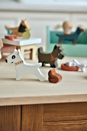 A wooden dog figure in white with a brown collar stands on a light-colored surface, surrounded by colorful dog toys and other animal figures, perfect for imaginative play.