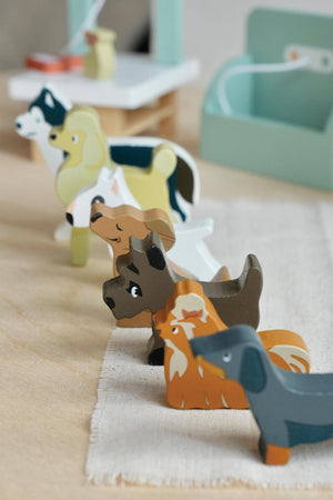 A row of colorful wooden dog figures in various breeds, including a Dachshund and a Husky, sits on a light fabric surface, showcasing the playful design of the Waggy Tails.