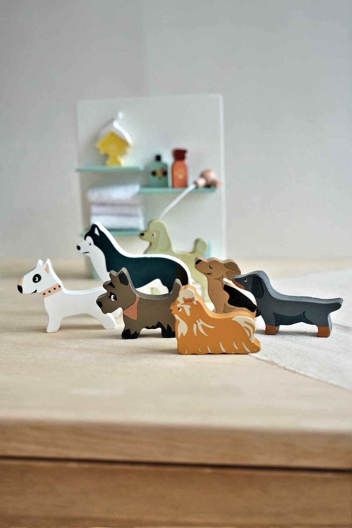 A collection of seven colorful wooden dog figures in various breeds, including a Dachshund and a Bull Terrier, set against a minimalistic grooming station background, perfect for imaginative play.