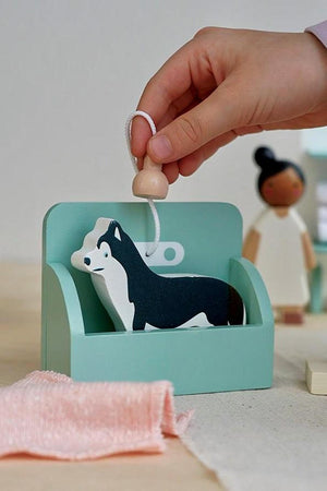 A child’s hand lifts a black and white wooden Husky dog from a mint green grooming station, showcasing the playful design of the Tender Leaf Wooden Toys grooming set.
