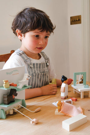 A young child plays with the Tender Leaf Wooden Toys Waggy Tails Dog Salon set, featuring a groomer and various dog figures, on a wooden table in a bright, inviting.